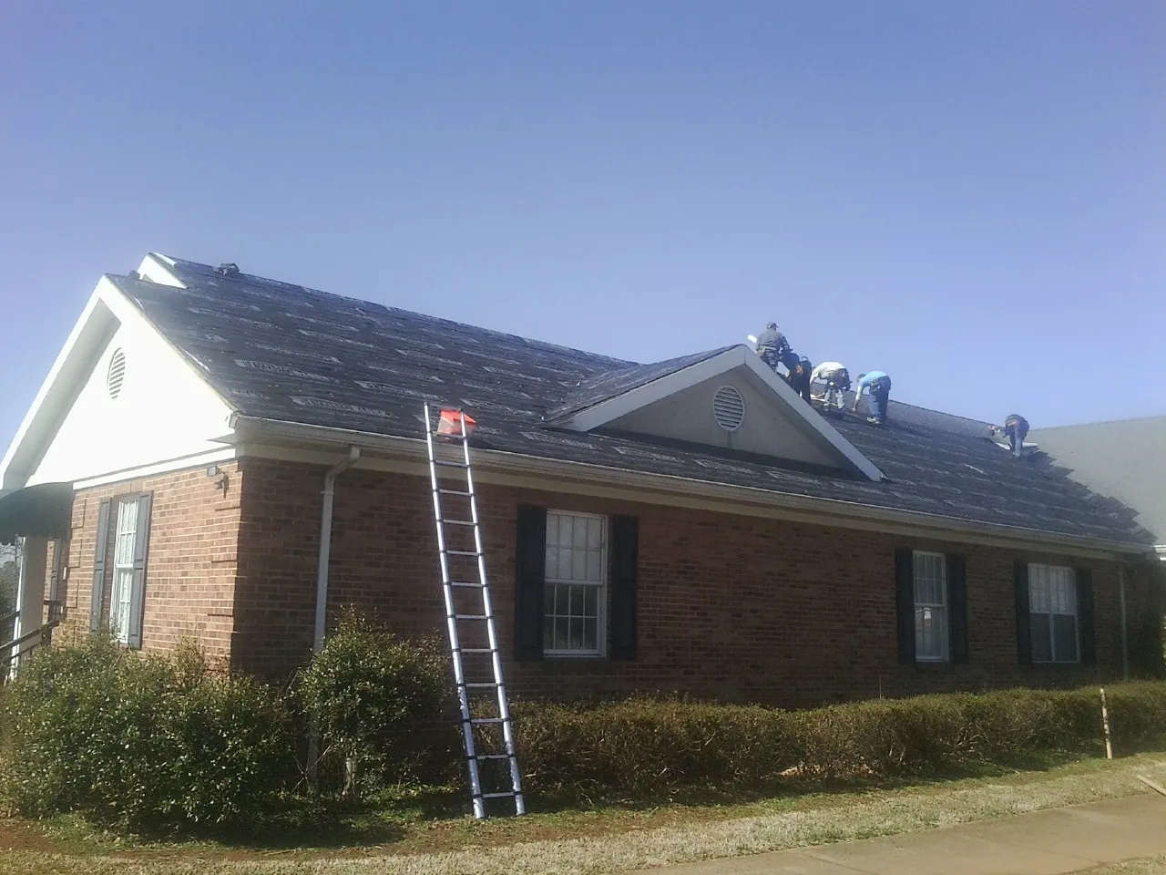 Crew tearing shingles off a brick ranch roof with a ladder set — Emergency Roof Repair work by our crew in North Aurora
