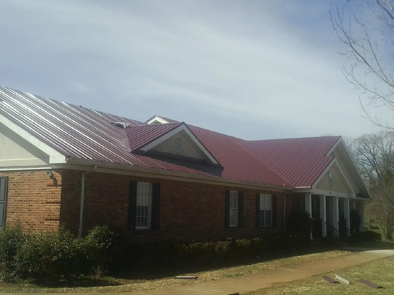 Red metal roof with gabled entries on a long brick building, from a Hail Damage Roof Repair job in North Aurora