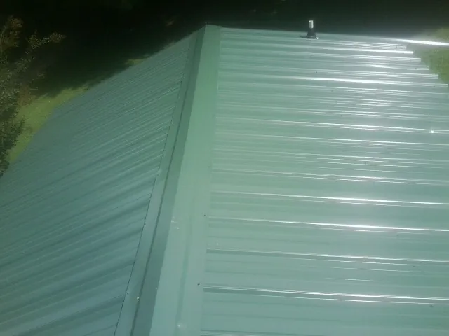 New green metal panels meeting at the ridge of a roof — Flat Roof Repair work by our crew in North Aurora