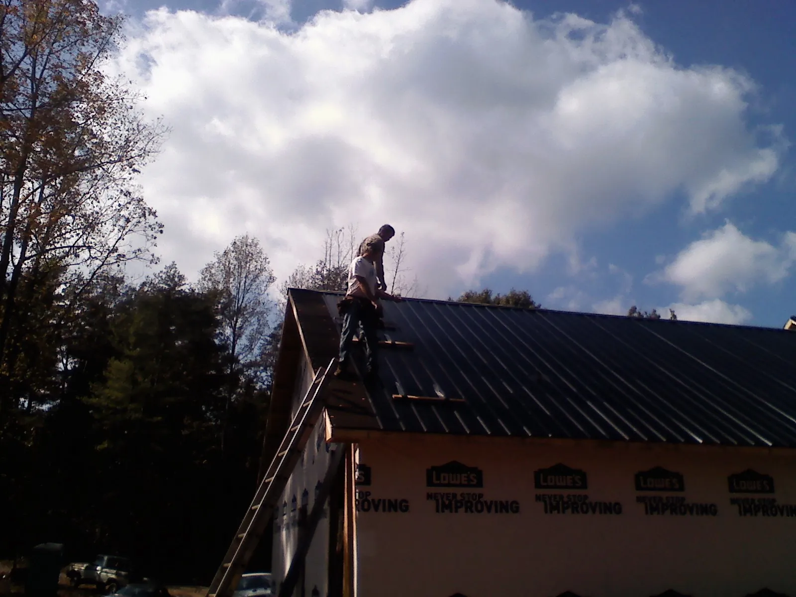 Roofer fastening dark metal panels high against a cloudy sky, from a Roof Inspection job in North Aurora