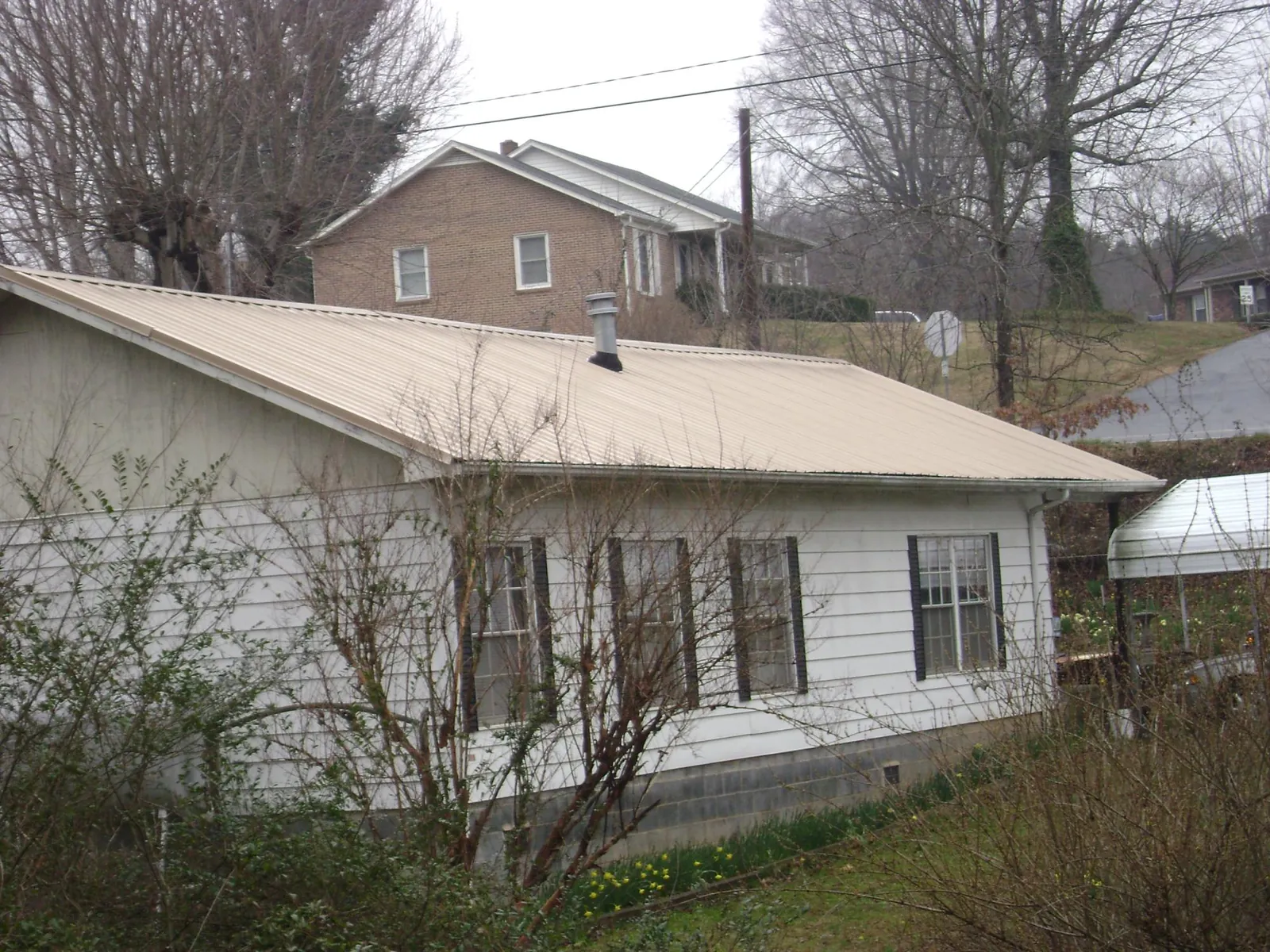 Tan metal roof on a white sided house set into a hillside in North Aurora